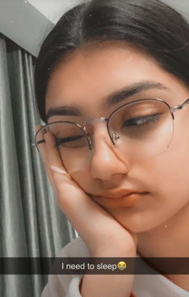 Girl resting her face on her hand with eyes nearly closed, wearing glasses, and the caption “I need to sleep 😭” overlaid.