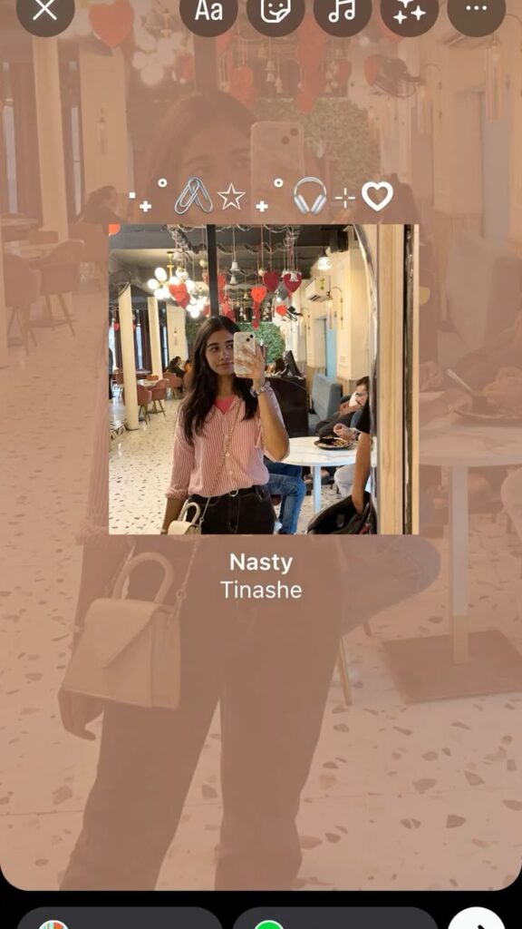 A mirror selfie layout for Instagram Stories, featuring a centered photo of a girl in a pink striped shirt with a music overlay ("Nasty" by Tinashe), layered over a blurred version of the same image to create a soft, minimal aesthetic.